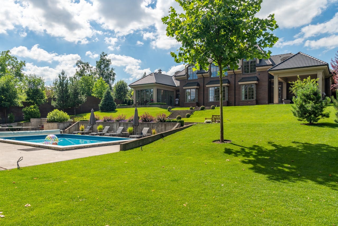Spacious elegant mansion with a pristine pool, lush garden, and clear blue sky.